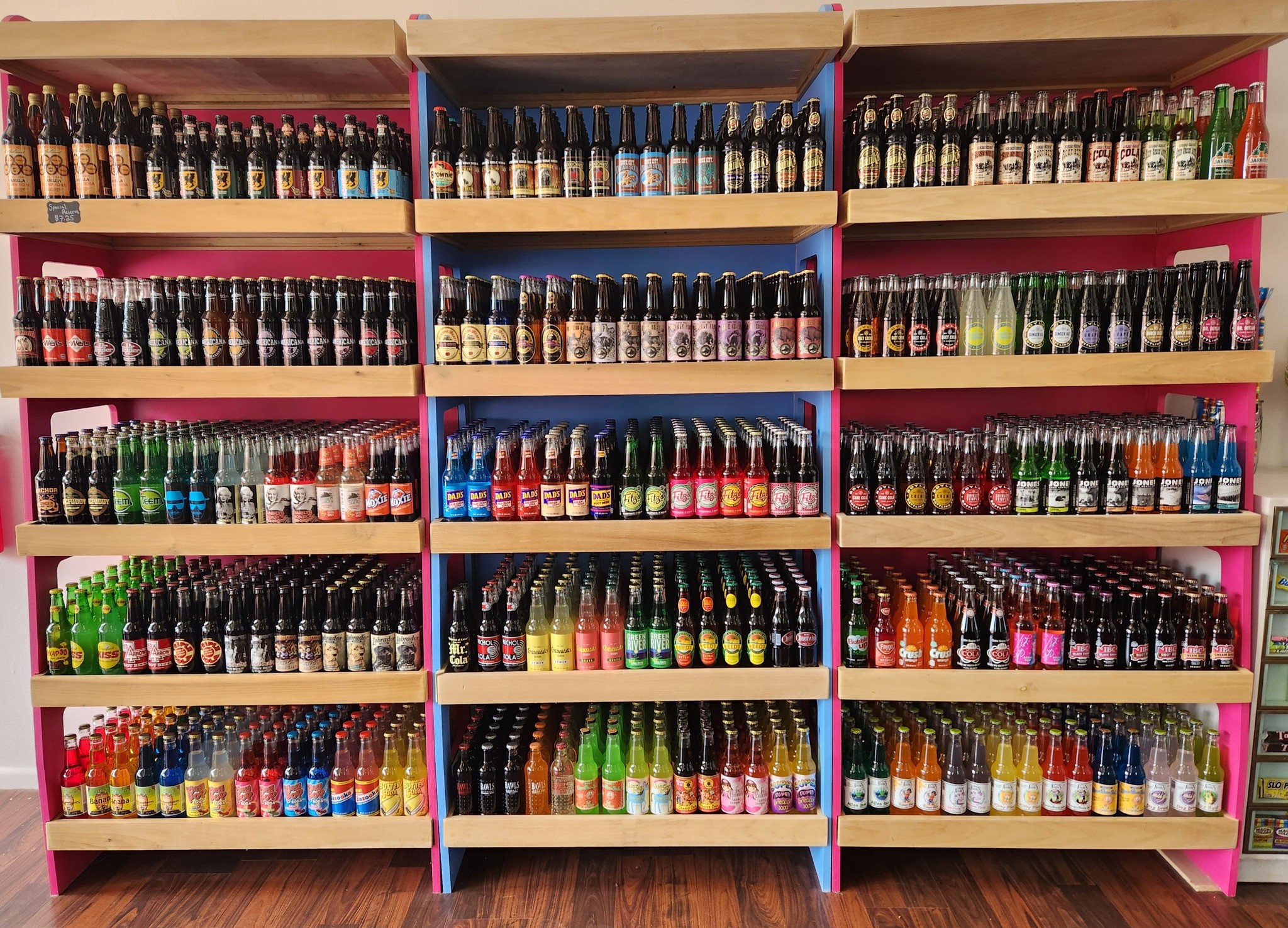 Colorful display of over a hundred glass-bottle sodas on bright shelves